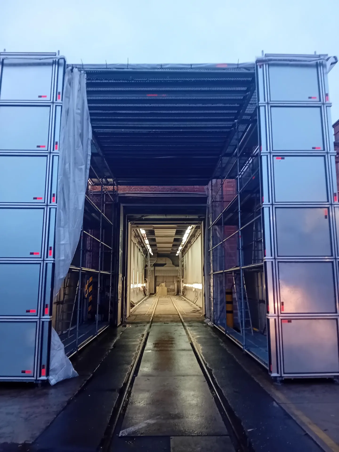 Blick durch die Einhausung mit Kassettenwänden auf die beleuchtete DB-Werkhalle, Breeser Straße Wittenberge