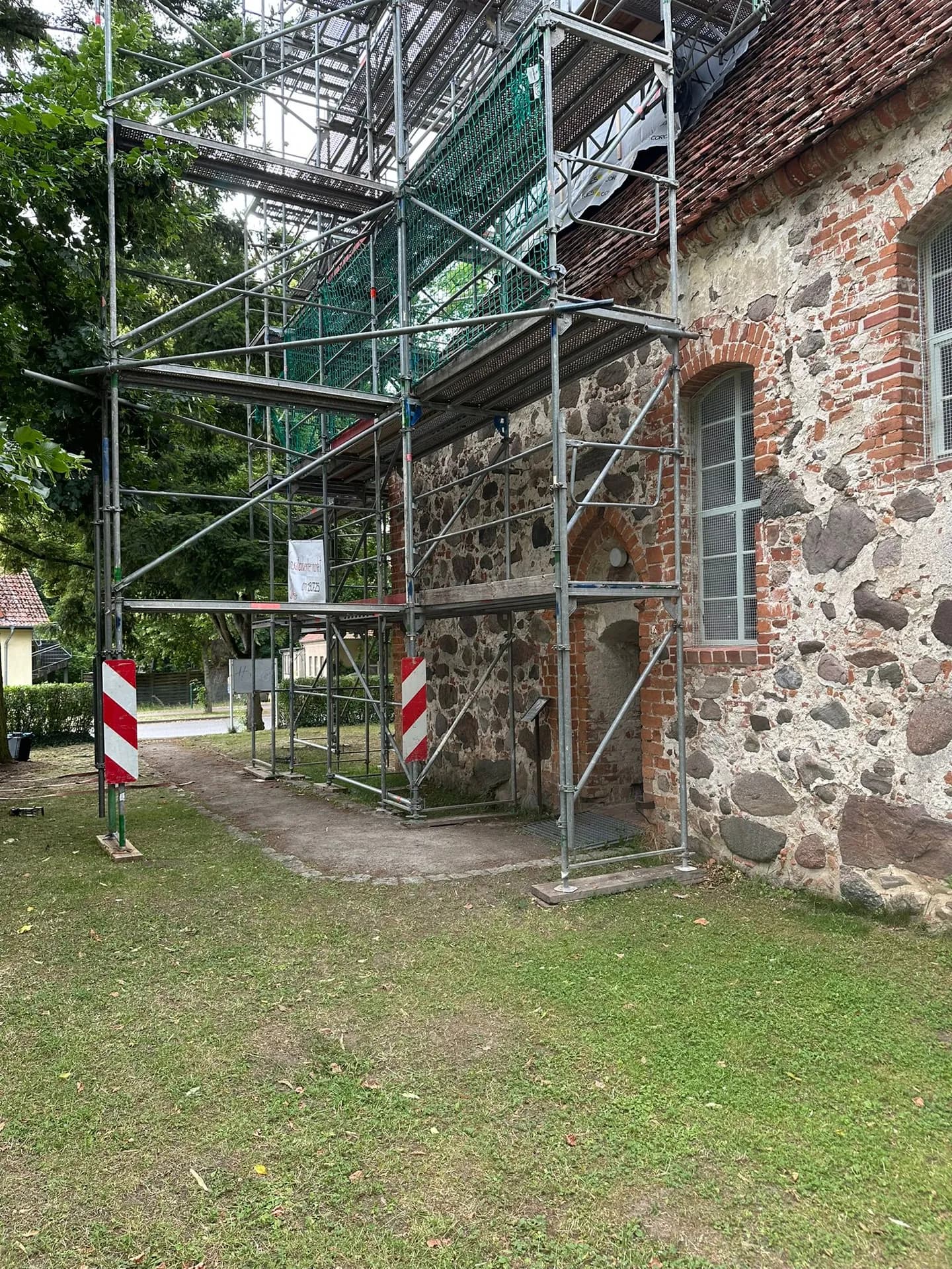 Gerüstdurchgang am Kirchenportal mit Schutznetz und Dachfangebene, Dorfkirche Gnewikow